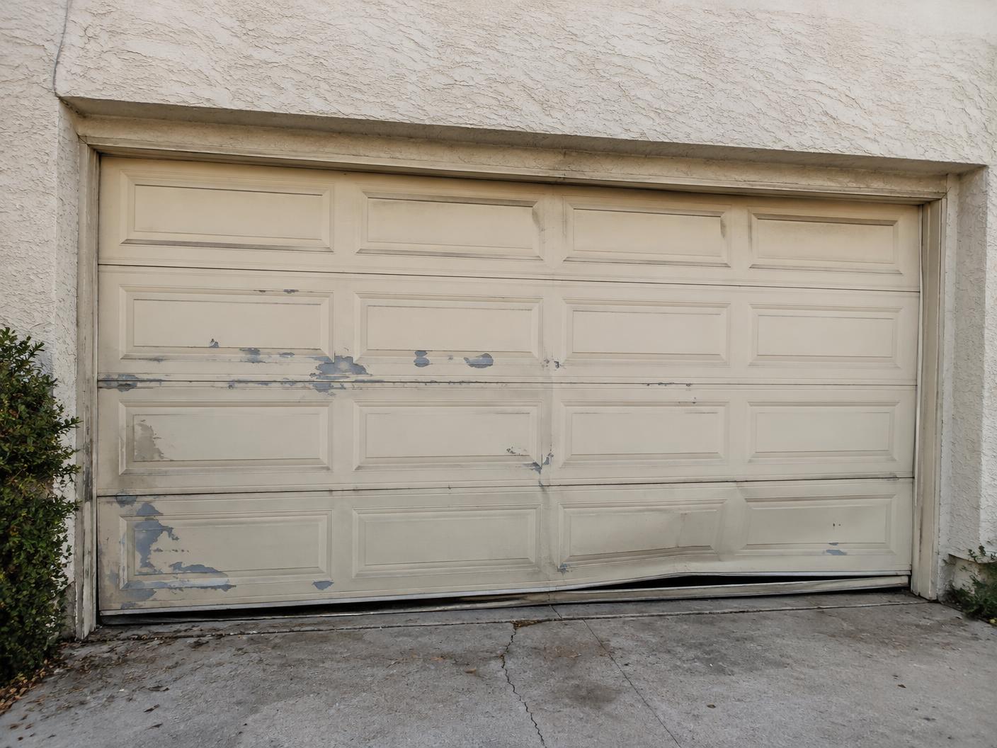 Dented beige garage door with peeling paint on a stucco home